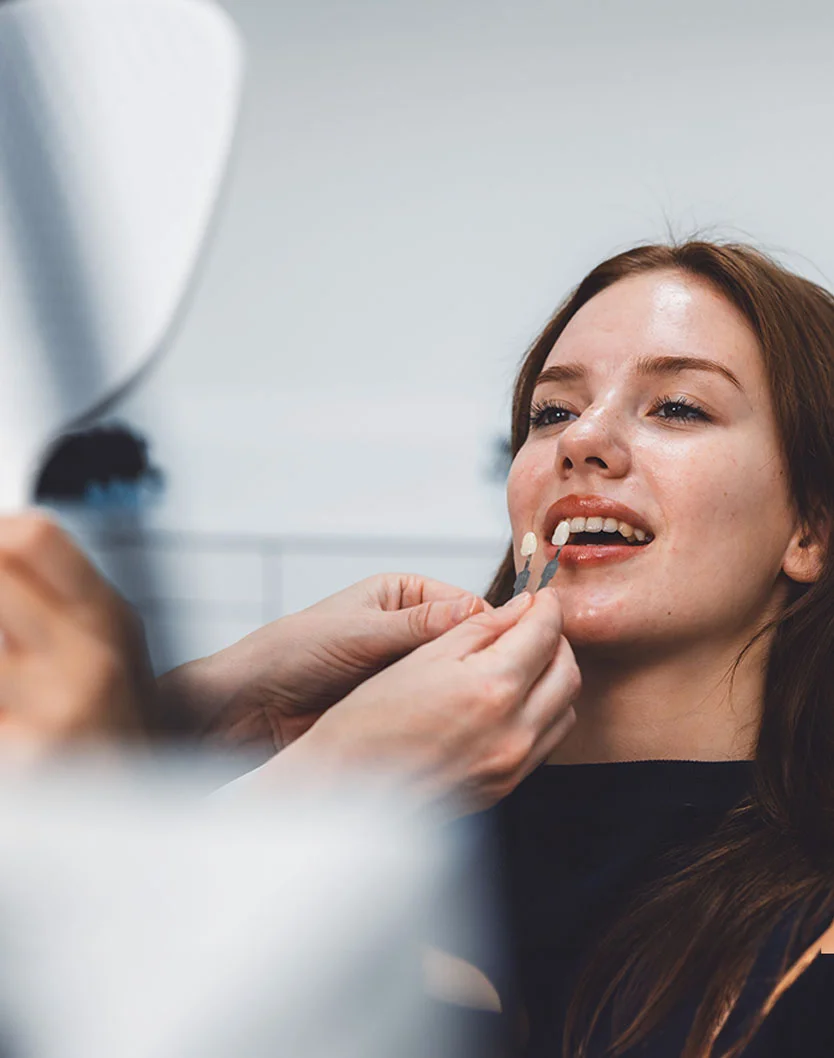 A close-up view of a dental patient engaged in a teeth whitening consultation. The patient smiles as they carefully consider various shade options while receiving guidance and assistance from a dental professional. - Veneers in Bakersfield, CA