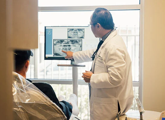 Dr.Huang pointing and looking at X-Ray images on his computer,mshowing his patient - Dentist in Bakersfield, CA