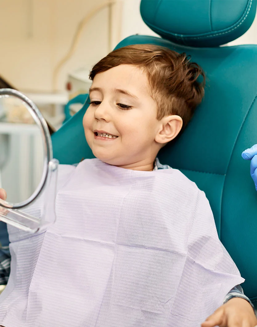 Young boy looking at his smile in a mirror at a dentist office - Pediatric Dentistry in Bakersfield, CA