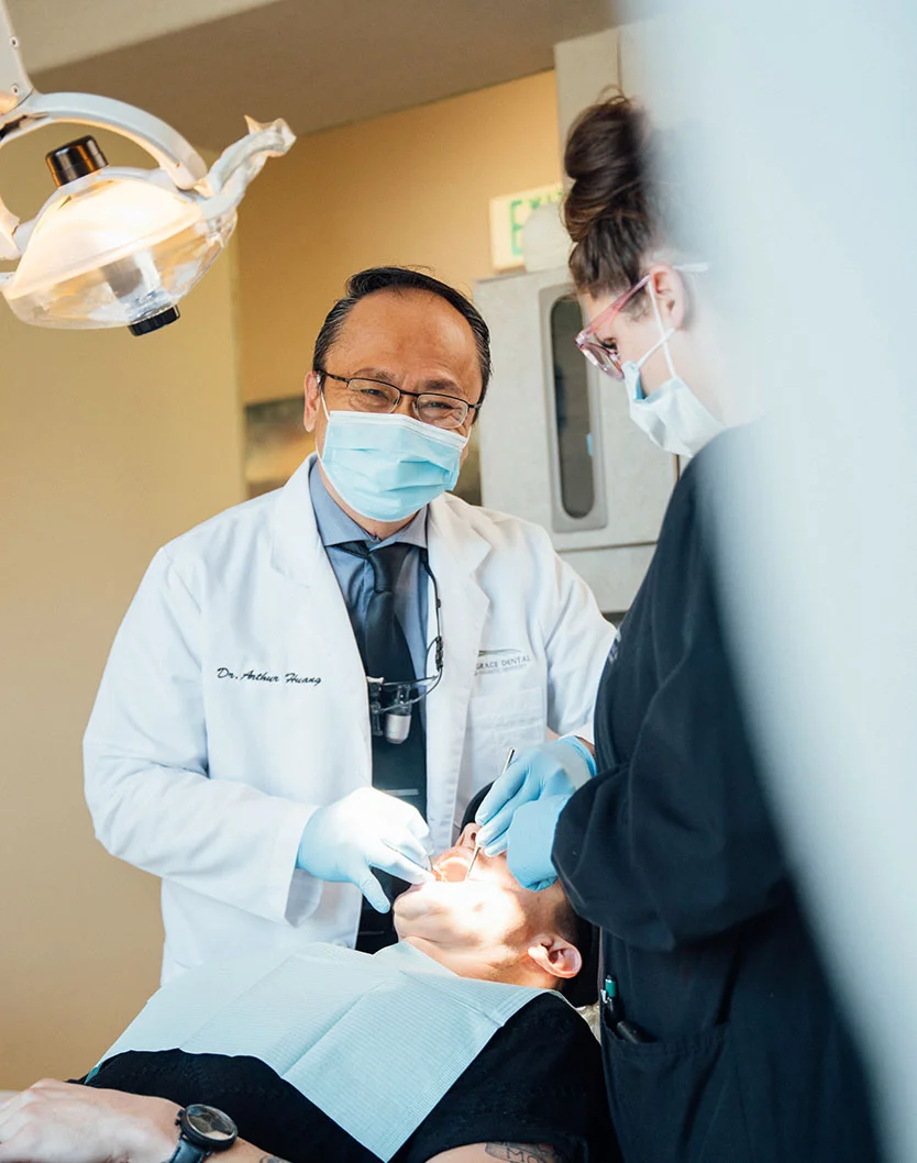 Dr.Huang smiling under his mask while giving a dental checkup to a patient, assisted by his nurse - Dental Selants in Bakersfield, CA